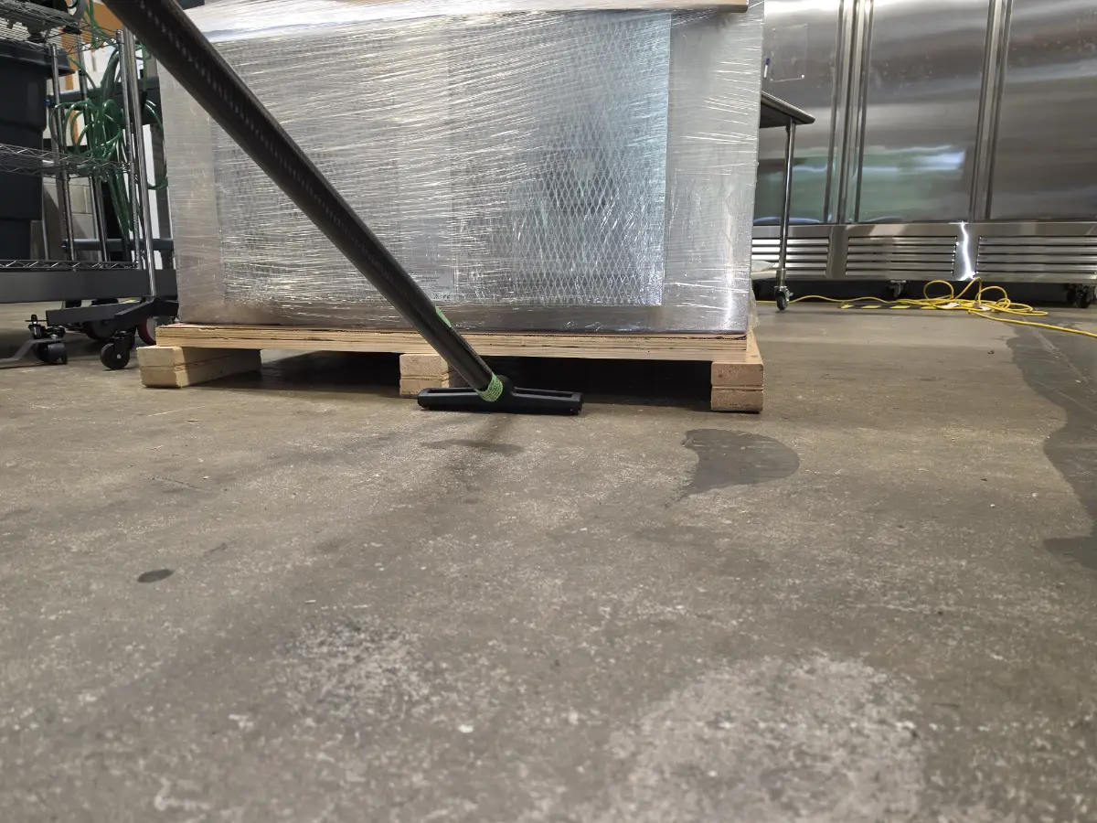 Dusting beneath a pallet in a warehouse with a specialized HEPA filtered vacuum